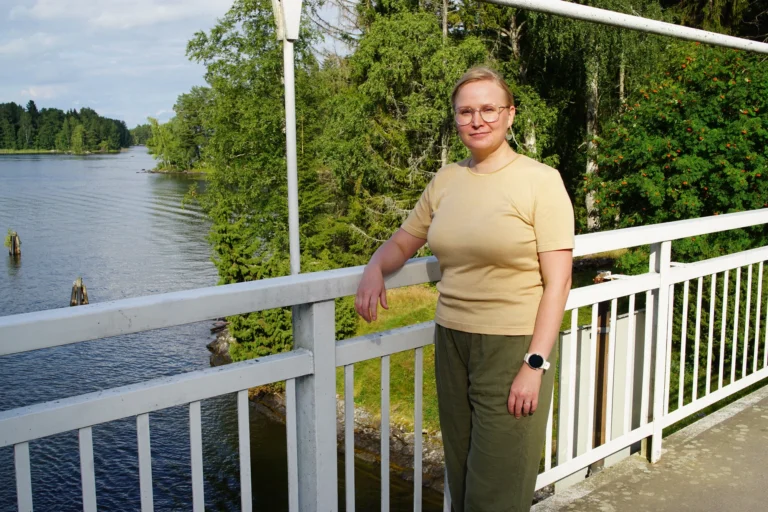 Hieroja nojaa sillan kaiteeseen, taustalla järvi ja kesäinen rantametsä